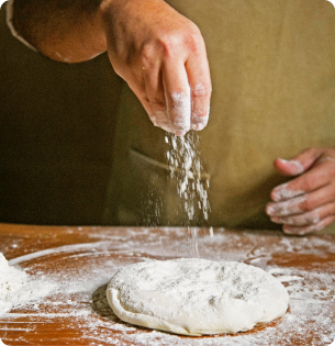 Mão polvilhando farinha sobre a massa de pizza na bancada